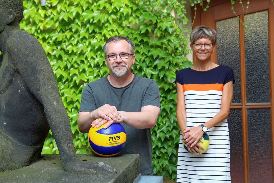 Foto: Zwei Beschäftigte des Hochschulsports der WHZ stehen vor einer berankten Wand. Holger Welt lehnt neben einer halb zu sehenden Skulptur auf einem Basketball, Ulrike Lemberg steht rechts hinter ihm mit einem Handball in den Händen.