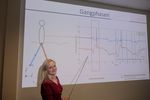 Foto: Eine junge Frau steht mit einem Zeigestock in der Hand vor einer Projektion, auf der ein Diagramm mit der Überschrift Gangphasen zu sehen ist