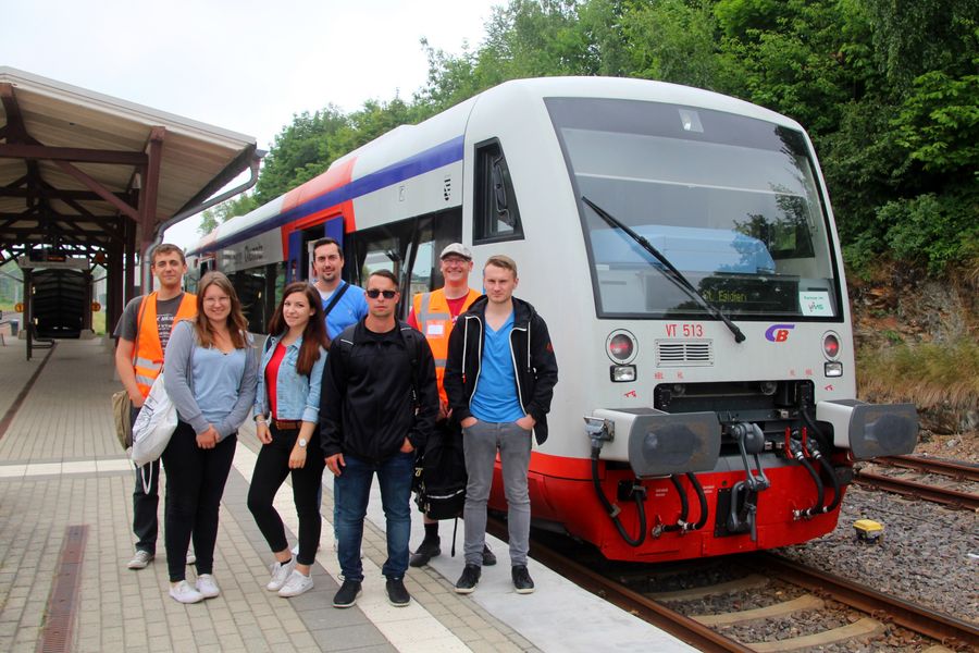 Foto: Gruppenbild auf einem Bahnsteig vor einem Triebwagen der Eisenbahn.