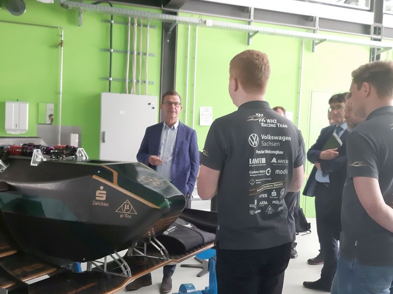 Foto: Ein Mann steht hinter einem Elektro-Rennauto und spricht mit Mitgliedern des WHZ-Racing Teams, die von hinten zu sehen sind. 
