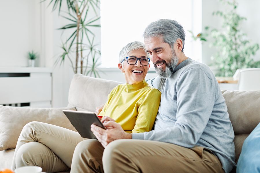 Mann und Frau sitzen auf der Couch und schauen auf ein Tablet.