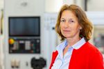Portraitfoto: Eine Frau schaut in die Kamera, im Hintergrund ist verschwommen eine Maschine.