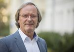 Foto: Peter Mietke blickt in die Kamera. Er trägt ein grau-blaues Sakko und ein weißes Hemd. Im Hintergrund sind unscharf Hochschulgebäude zu sehen.