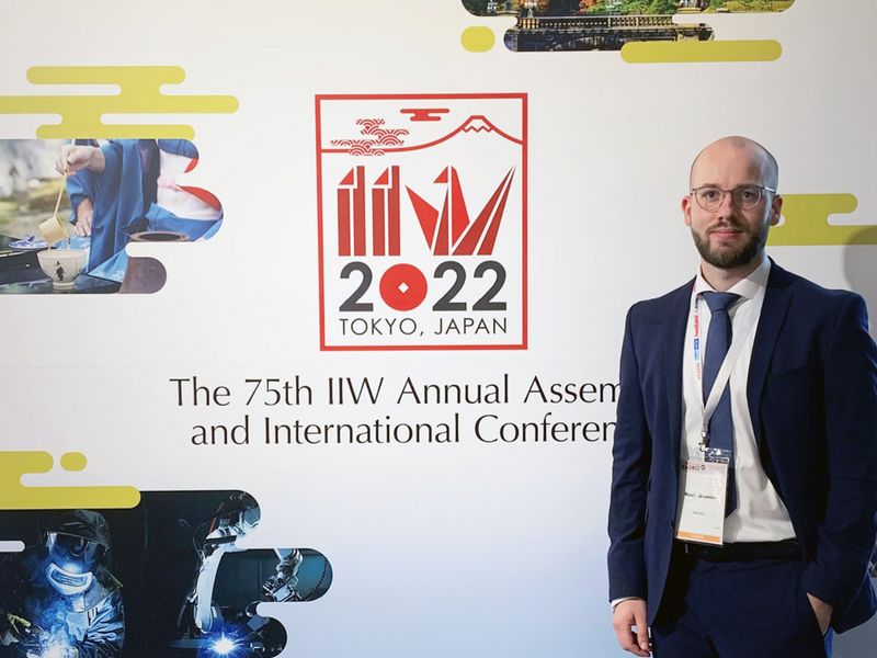 Mitarbeiter der AMB steht vor dem Logo der 75th IIW Annual Assembly and International Conference in Tokio