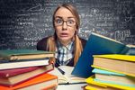 Foto: Eine Studentin sitzt verzweifelt zwischen vielen Büchern und vor einer Tafel mit Formeln.