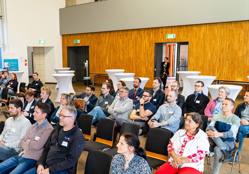 Menschen sitzen auf Stuhlreihen und blicken auf die Bühne