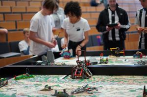 Ein Spielfeld mit Lego-Robotern, dahinter PErsonen und ein Hörsaal