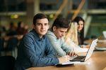 Junger Mann sitzt in Bibliothek am Laptop