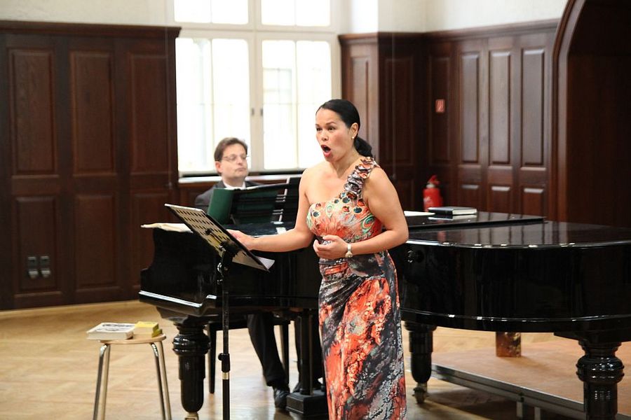 Foto: Ein Mann sitzend am Klavier spielend. Im Vordergrund eine Sängerin stehend und singend.