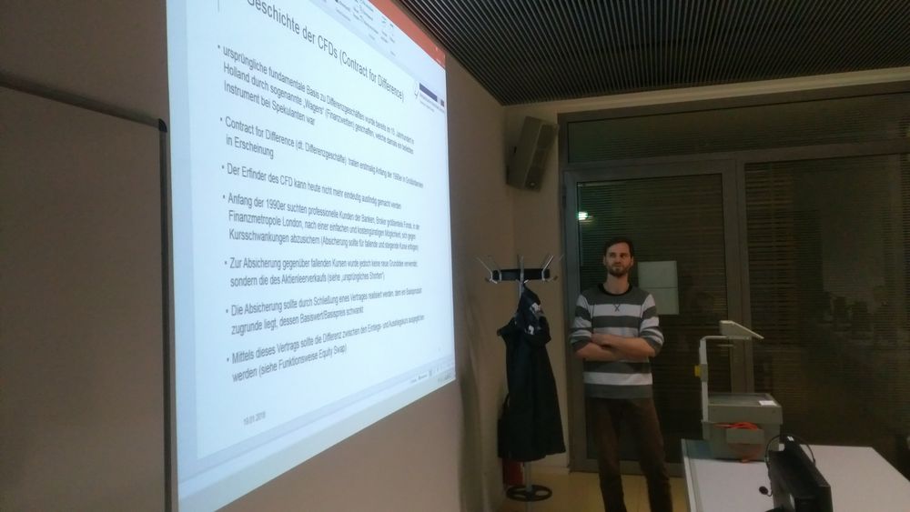 Foto: Ein Gastreferent referierte zum Thema CFDs und Kryptowährung. An einer Wand wird eine Präsentation mit Textinhalt gezeigt.en