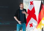 junger Mann hält einen Vortrag, im Hintergrund ist die deutsche und die georgische Flagge zu sehen