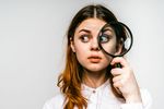 Foto: Ein junges Mädchen dreht die Augen seitlich und hält vor einem Auge eine große Lupe.