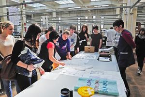 Foto: Besucher stehen um einen Stand und betrachten verschiedene Stoffe. Textiles "Begreifen" im Technikum des ITL. Bildquelle: Susanne Baumung