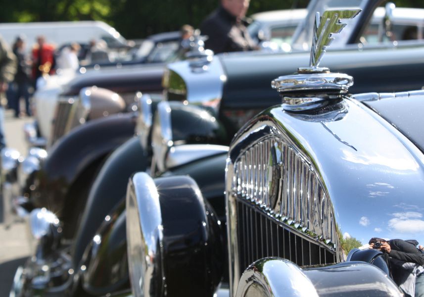 Der Kühlergrill eines Oldtimers. Im Hintergrund weitere Fahrzeuge. 