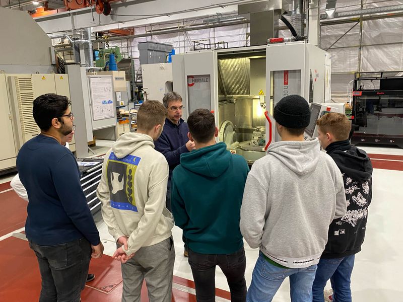 Gruppe von Schülern im Labor stehen um Mitarbeiter, der die Maschine erklärt