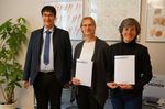 Foto: Neben einem Mann stehen zwei Frauen, die beide eine Urkunde in der Hand halten.