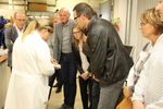 Eine Frau in einem weißen Kittel zeigt einer Gruppe interessierter Männer und Frauen das Produkt eines chemischen Versuchs.