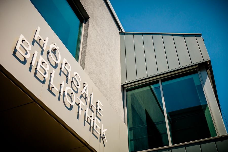 Foto: Eingang zu einem Lehrgebäude. Schrift über Eingang: Hörsäle, Bibliothek