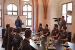 Personen sitzen in einem festlichen Raum an einer gedeckten Tafel, Oberbürgerrmeisterin spricht, eine Kamera filmt das Geschehen.