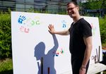 junger Mannim schwarzen T-Shirt mit Brille hinterlässt bunten Handabdruck auf weißem Plakat