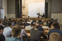 Foto: Teilnehmer sitzen in der Aula Scheffelberg. Auf der Bühne spielt ein Duett.