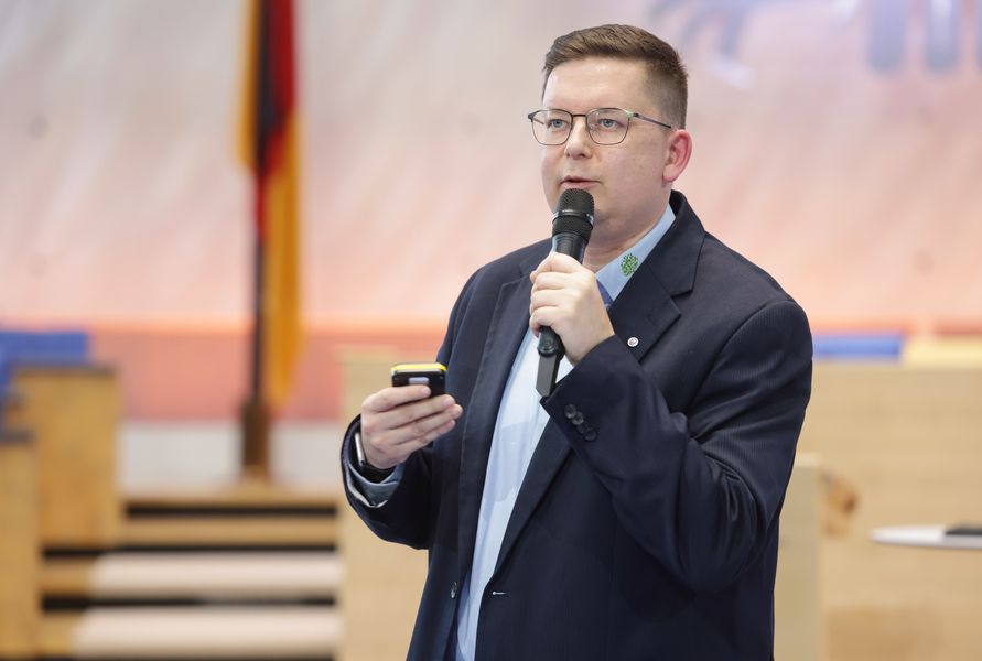 Eine Person spricht auf einer Bühne in ein Mikrophon. 