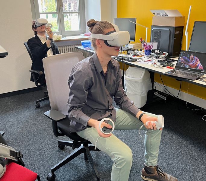 Person sitzt mit VR-Brille auf einem Drehstuhl in einem Büro. 