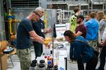 Personen experimentieren in einem Labor mit Chemikalien, andere Personen schauen ihnen dabei zu.