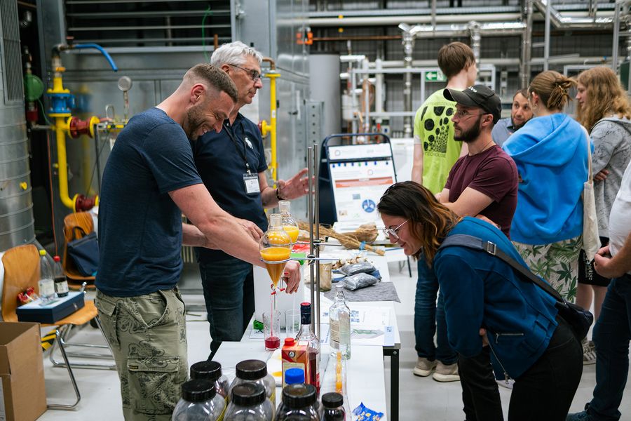 Personen experimentieren in einem Labor mit Chemikalien, andere Personen schauen ihnen dabei zu. 