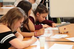 Foto: Drei Schülerinnen sitzen an einem Tisch und studieren jeweils einen vorliegenden Schriftsatz.