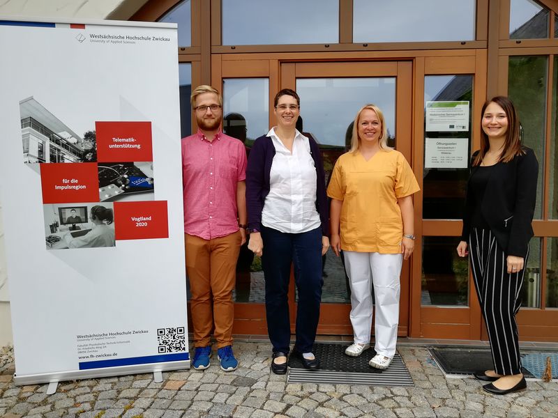 Foto: Gruppenbild mit 4 Personen. Vor einem Eingang der medizinischen Servicestelle stehend.