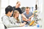 Foto: 3 Interessierte des Schnupperstudiums sitzen an einem Labortisch in der Elektrotechnik. Ein Mitarbeiter erklärt die Geräte.