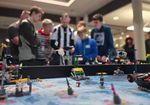 Personen stehen hinter einem Lego-Spieltisch, auf dem sich Roboter bewegen und Aufgaben lösen.