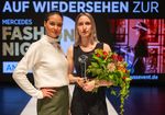 Sophie Stramek mit Blumenstrauß, neben ihr ein Modell, das ihre Kollektion trägt. Beide stehen auf einem Laufsteg.