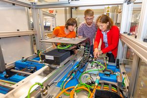 Foto: Zwei Studierende und eine Lehrbeauftragte an einem Demonstrator zur Mechatronik Ausbildung.