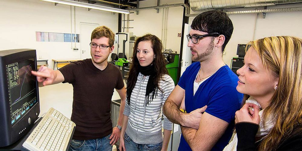 Photo: A student shows three other students a graphic representation with two curves and numerical values on a screen. source: whz/H. Gerischer