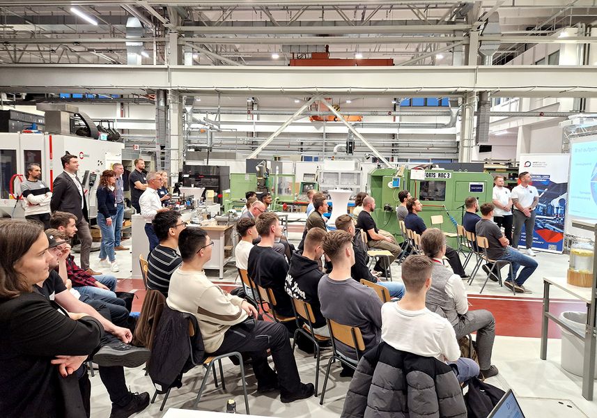 Studierende sitzen in einer Werkhalle und verfolgen einen Vortrag. 