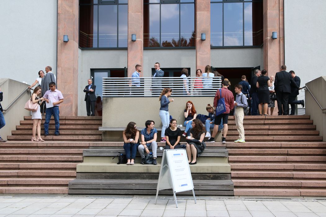 Foto: Teilnehmer sitzen und stehen auf der Treppe vor der Aula.