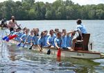 Team aus Männern und Frauen in hellen T-Shirts auf einem Teich im Drachenboot