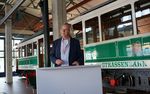 Dr. Peter Mietke steht an einem Rednerpult, im Hintergrund ist eine historische STraßenbahn zu sehen.