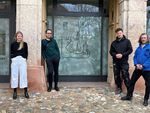 Foto: Vier Personen stehen vor einem künstlerisch gestaltetem Fenster.