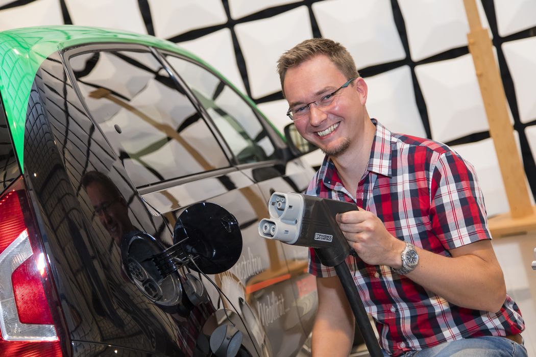 Foto: Thomas Opp mit Ladestecker in der Hand neben einem Elektroauto.