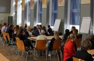 Foto: Studierende und Gäste sitzen in Gruppen in der Aula Scheffelberg und unterhalten sich.