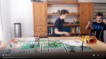 Foto: Im Vordergrund steht eine Lego-Fläche, im Hintergrund bewegen sich zwei Jungen während des Robot Games.