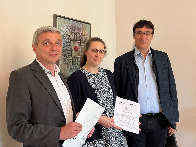 Foto: Eine Frau und zwei Männer haben einen Vertrag in der Hand. 