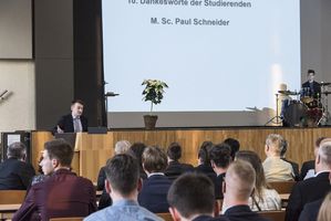 Foto: Absolventen sitzen in der Aula Scheffelberg. Am Rednerpult M. Sc. Paul Schneider.