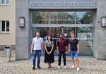 vier junge Forscher, davon eine Frau, stehen vor einer Hochschule und schauen in die Kamera