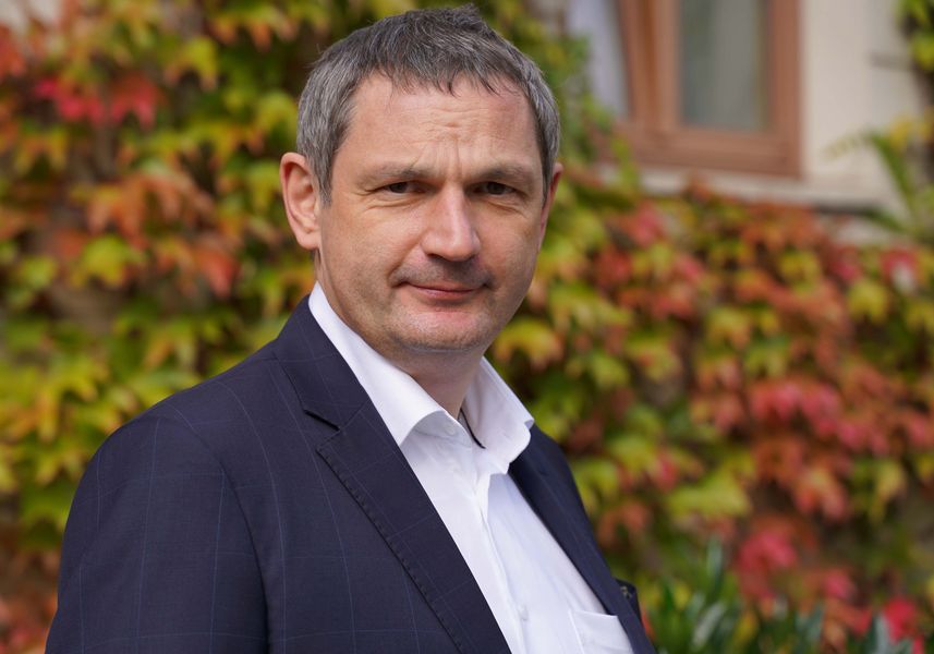 Foto: Prof. Zitzelsberger schaut in die Kamera. Er trägt dunkles Sakko und weißes Hemd. 