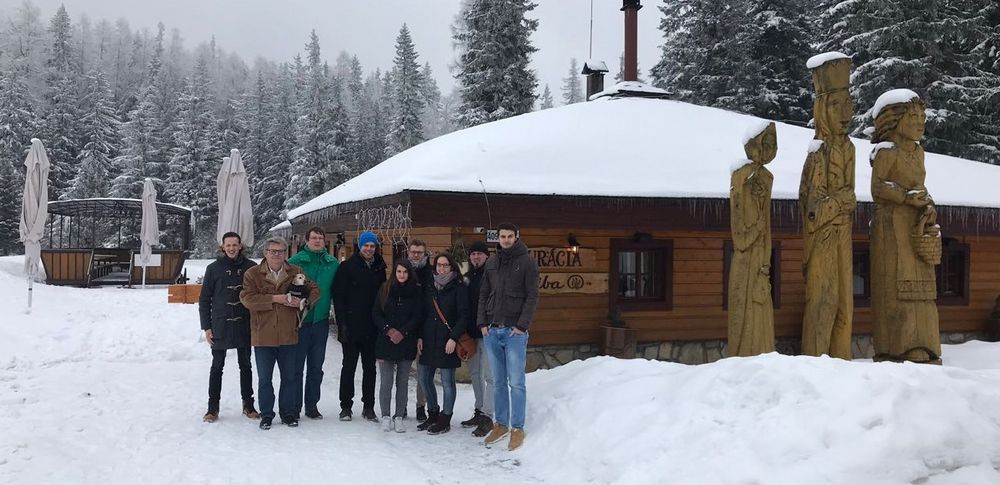 Gruppenfoto: Eine Gruppe Studierender steht vor einer Holzhütte im Wald. 