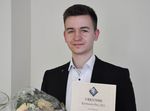 Foto: EIn lächelnder junger Mann hält eine Urkunde in der Hand.